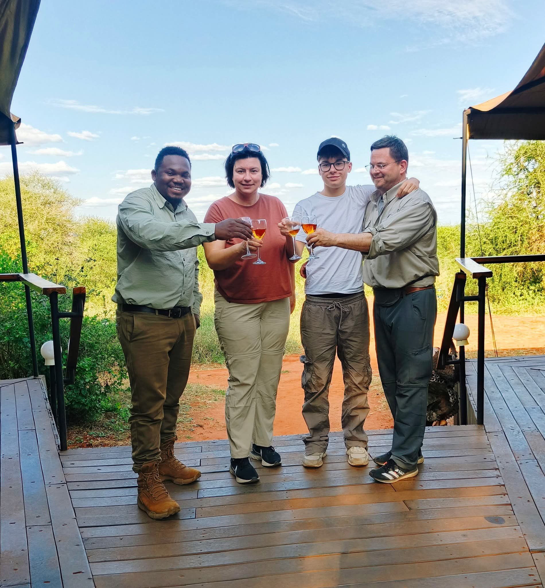 Safari guide and guests beside a Land Cruiser on a dusty track at golden hour