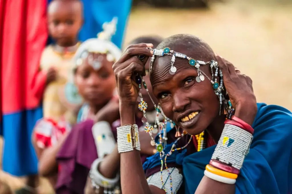 A smiling Maasai girl in beaded jewellery with children behind her